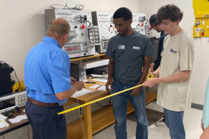 SEED Program: Students and an instructor measuring a popsicle stick bridge in class.